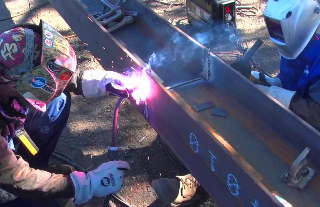 Imagen de un soldador y su ayudante soldando dos vigas de acero mediante el proceso de soldadura de doble escudo - Aplicaciones